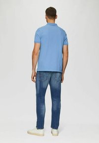 Hellblaues Polo-Shirt mit kurzen Ärmeln, kombiniert mit dunkelblauen Jeans. Das Modell trägt weiße Turnschuhe und wird von hinten gezeigt.