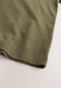 Tricou din material textil verde măsliniu cu textură fină, având o margine curată și detalii subtile de cusături pe margini.