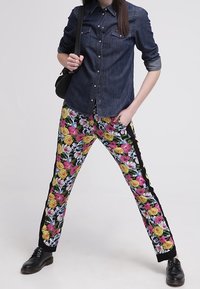 Donkerdenim overhemd met knopen en zakken, gecombineerd met zwarte bloemenbroek met grote roze en gele rozen en zwarte zijkanten.