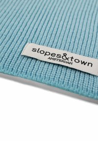 Tessuto a righe di colore azzurro chiaro con una consistenza morbida, caratterizzato da un'etichetta bianca con la scritta "slopes&town AMSTERDAM" stampata in nero.