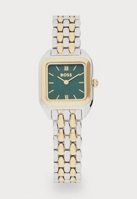 Montre rectangulaire dorée et argentée avec un cadran vert, index des heures dorés et marque Boss ; elle possède un bracelet en maillons.