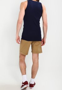 Débardeur bleu marine à la coupe ajustée associé à un short kaki mi-long. Des chaussettes blanches aux chevilles et des baskets bordeaux complètent le look.