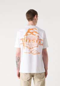 T-shirt bianca con una grande grafica arancione sul retro, con testo e motivi di fiamme. Maniche corte e vestibilità rilassata.