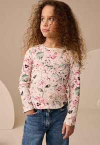 Bluză cu mânecă lungă din țesătură ribbed roz, cu un model floral; asortată cu blugi din denim albastru. Dispune de un decolteu rotund și mâneci ajustate.
