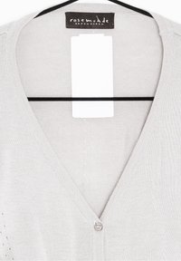 Ljust grå cardigan med V-hals, mjuk textur, knäppning och räfflade detaljer längs kanterna. Etikett synlig vid halsringningen.