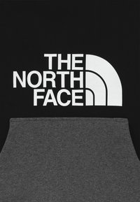 Svart hoodie med en stor vit logotyp av "THE NORTH FACE" och en grå nederdel med mjuk textur och enkel design.
