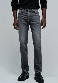 Jeans negros en un lavado medio, de corte recto, con cinco bolsillos, costuras en contraste y una clásica bragueta con botones. Combinados con zapatos negros.