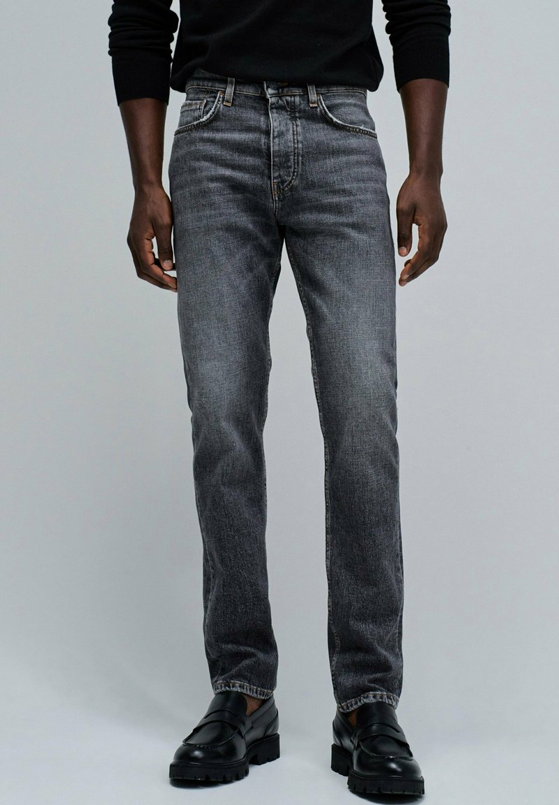 Jeans negros en un lavado medio, de corte recto, con cinco bolsillos, costuras en contraste y una clásica bragueta con botones. Combinados con zapatos negros.