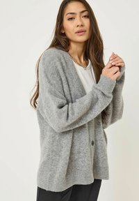Grå stickad cardigan med en avslappnad passform, långa ärmar och kn�äppning med knappar. Mjuk textur och ribbade mudd, lager över en vit topp.