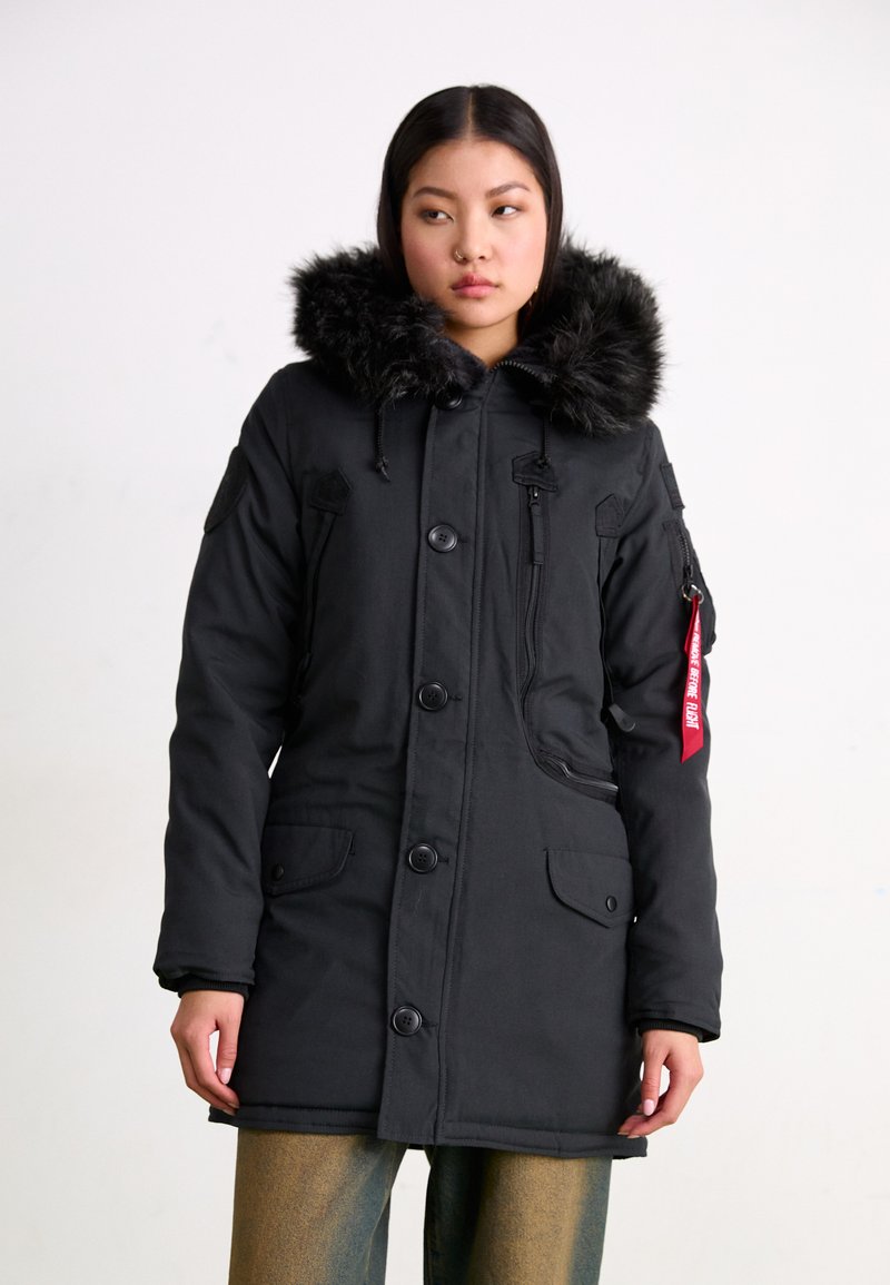 Čierny parka kabát s umelým kožuchom na kapucni, so zapínaním na gombíky a zips, bočnými vreckami a červenou nášivkou; má priliehavý strih a elegantný dizajn.