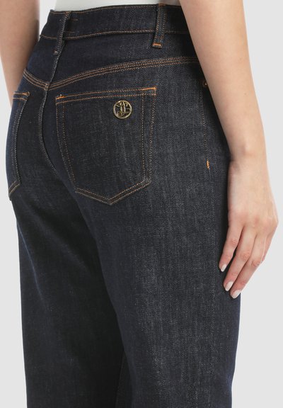 Donkerblauwe denim jeans met een strakke tailleband en een gouden logo op de achterzak. Voorzien van oranje stiksels en een standaard ontwerp voor de achterzak.