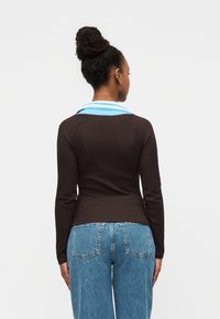 Καφέ πουκάμισο με μακριά μανίκια και γιακά με γαλάζιες ρίγες, συνδυασμένο με ψηλόμεσο τζιν παντελόνι σε μπλε χρώμα. Διαθέτει εφαρμοστή γραμμή και μανίκια ράγκλαν.