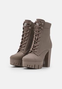 Bottines marron en similicuir avec bout rond, devant à lacets, plateforme épaisse et talon haut. Présentent des accents surpiqués et un détail logo.