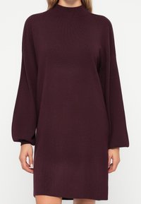 Robe ample à manches longues en maille bordeaux foncé. Col montant, coupe décontractée, texture côtelée et manches légèrement évasées.