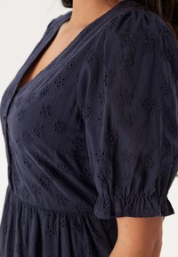 Abito in cotone blu navy con maniche a sbuffo, ricamo floreale con occhiello e design con bottoni sulla parte frontale, con vita arricciata.