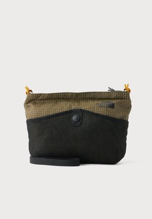 Lille crossbody taske i olivengrønt og sort stof, gule lynlåse og en sort justerbar rem på hvid baggrund.