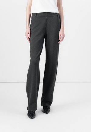 Person wearing dark gray wide-leg trousers paired with black pointed-toe shoes and a white top, standing against a white background.