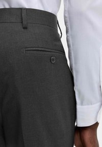 Mørkegrå skræddersyede bukser med en sidelomme og knapdetalje, parret med en strøget hvid skjorte med en glat tekstur.