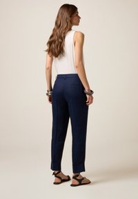 Pantaloni in lino navy con vestibilità rilassata, gamba affusolata e orli risvoltati, abbinati a una maglietta senza maniche bianca e sandali neri.