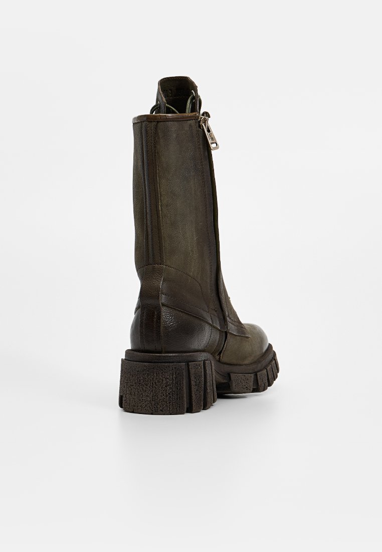 Bottines en cuir vert olive avec une semelle épaisse et texturée, fermeture éclair sur le côté et finition mate. Présente des textures lisses et légèrement usées.
