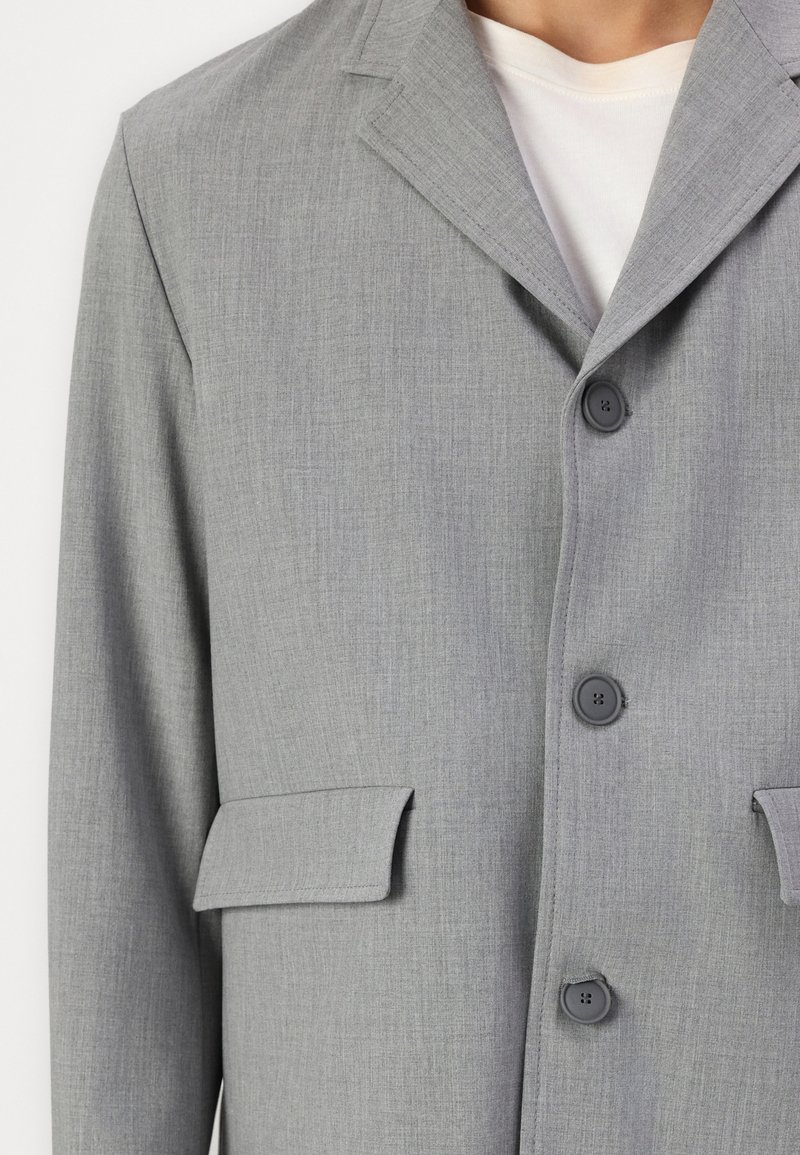 Jasnoszara marynarka z teksturowej tkaniny, z klapami w kształcie notcha, dwoma przednimi kieszeniami naszytymi oraz ciemnymi guzikami do zapięcia.