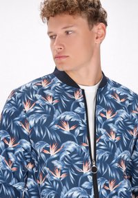 Giubbotto bomber blu con stampa di foglie tropicali, caratterizzato da accenti arancioni e rosa, colletto a costine e zip frontale. Tessuto dalla consistenza liscia.