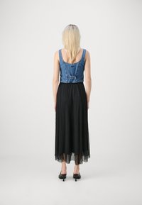 Kuttet denim topp med justerbar spenne, kombinert med en lang, plisserte svart skjørt. Antrekket har en myk tekstur og flytende design.