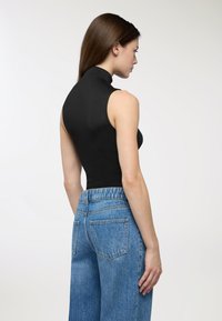 Top nero senza maniche con collo alto abbinato a jeans a gamba larga blu chiaro a vita alta. Texture liscia, design minimale, che mette in risalto una silhouette aderente.
