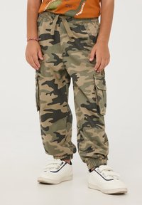 Pantaloni cargo mimetici in verde e beige con polsini elastici, vita regolabile con cordoncino e tasche laterali per riporre oggetti.