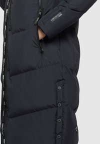 Giacca a vento nera con mano nella tasca con zip, zip con marchio, dettagli a bottoni lungo il lato e logo sulla manica e sull'orlo.