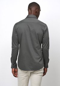 Grijze langemouwen shirt met een achterste yoke-detail en knoopmanchetten, gemaakt van een gladde stof, gepresenteerd op een witte achtergrond.