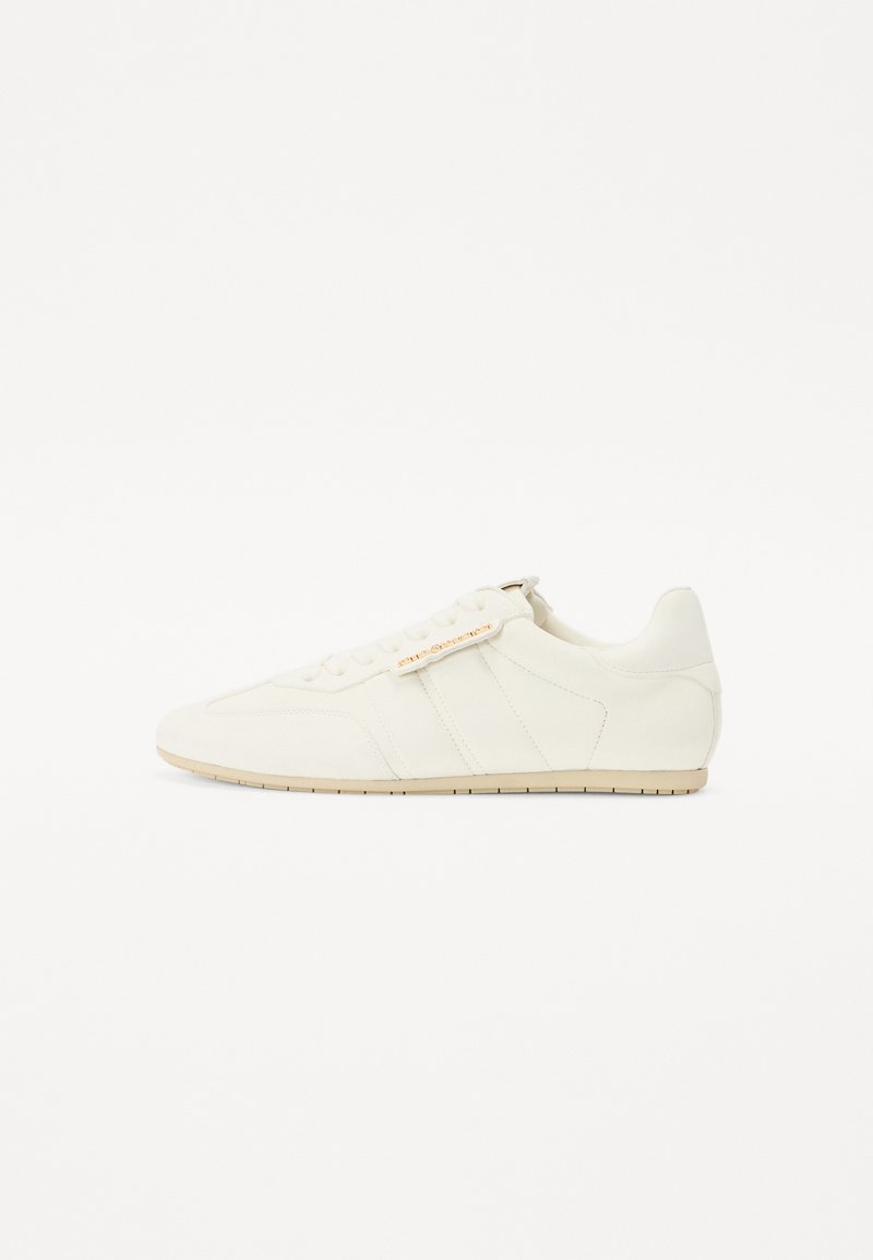 Sneaker bianco con tomaia in pelle liscia e suede, caratterizzato da tre strisce laterali, una punta arrotondata, lacci e una suola con texture.