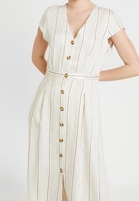 Light beige dress with vertical stripes in dark red. Features a deep V-neck, short sleeves, a cinched waist, and gold buttons down the front.