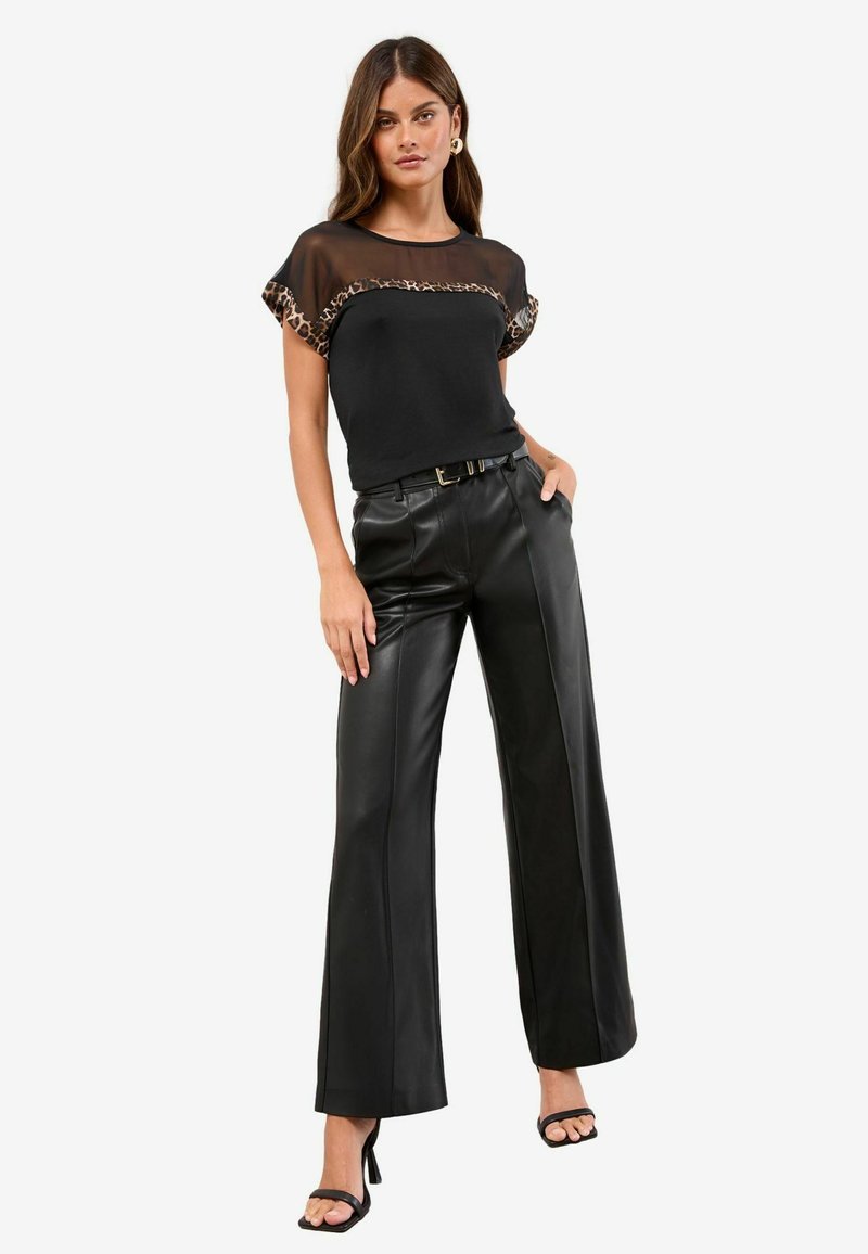 Mustat yläosat, joissa on läpikuultavaa leopardi-kohokuvioista reunusta, yhdistettyinä korkeavyötäröisiin mustiin keinonahkaisii leveisiin housuihin ja naruilla varustettuihin mustiin korkokenkiin.