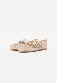 Gouden ballet flats met een gestructureerd patroon, versierd met kleine studs, kruisbanden en decoratieve accenten aan de zijkant. Zacht materiaal.