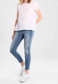 Top peplum corto de manga corta blanca combinado con jeans skinny desgastados de color azul claro y zapatillas blancas. El atuendo presenta un ajuste casual y relajado.