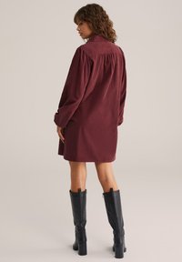 Burgundia värvi korduroy kleit krae, pikad puhvärvid ja voldid seljas, koos mustade kõrge kontsaga saapadega kuni põlveni.