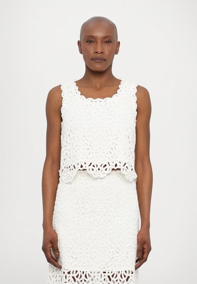 Top crop en crochet blanc avec un ourlet festonné, associé à une jupe assortie. Présente des motifs floraux complexes et un tissu texturé.