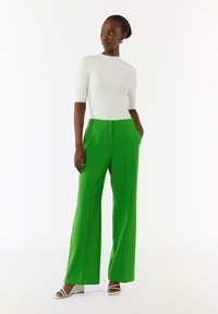 Zielone spodnie w szerokim kroju wykonane z gładkiego materiału, z wysokim stanem i przednimi kieszeniami, zestawione z dopasowaną białą bluzką z krótkim rękawem.