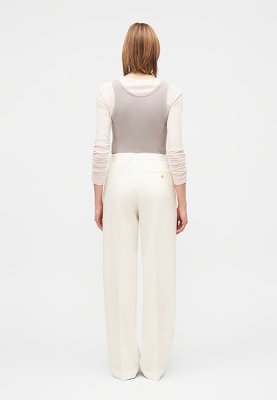 Šviesiai pilkas rausvų briaunų marškinėliai, apsivilkti virš ilgomis rankovėmis kremo spalvos marškinėlių, derinami su aukšto liemens, plačiomis baltomis kelnėmis su galine kišene.