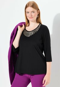 Zwarte top met een ronde halslijn en metallic versieringen, gecombineerd met paarse broek, met driekwartmouwen en een gladde textuur.