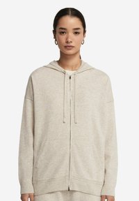 Ljus beige zip-up hoodie med dragsko i huvan, ribbade ärmslut och nederkant. Mjuk textur och två framfickor. Enkelt, utan dekorationer.