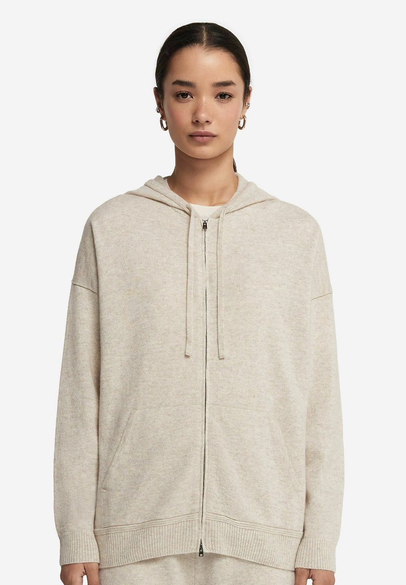 Ljus beige zip-up hoodie med dragsko i huvan, ribbade ärmslut och nederkant. Mjuk textur och två framfickor. Enkelt, utan dekorationer.