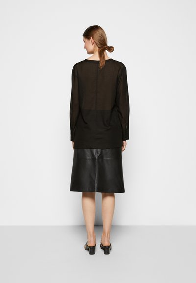 Blusa preta transparente de manga longa combinada com uma saia de couro preta. Apresenta uma textura suave, corte descontraído, com uma costura nas costas ao longo do centro.