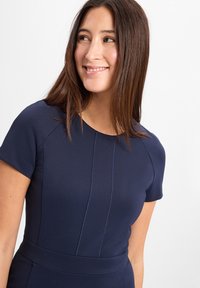 Marineblaues Kleid mit kurzen Ärmeln, rundem Ausschnitt und vertikalen Nahtdetails. Die glatte Textur und die taillierte Silhouette unterstreichen das Design.