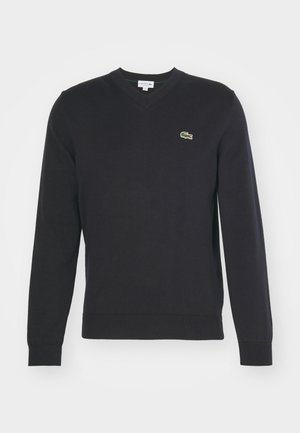 Sort bomuldsstrik sweater med V-hals, lange ærmer og ribbede manchetter. Har et lille grønt Lacoste-logo på brystet.