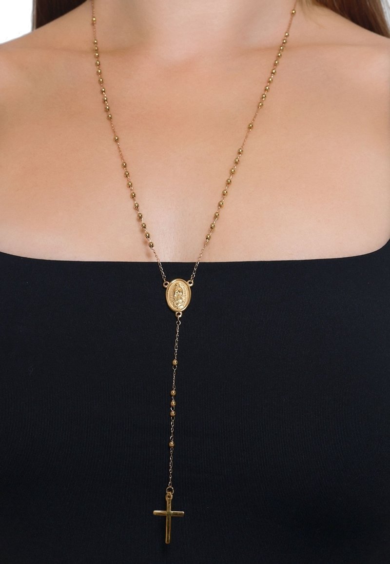 Collier chapelet en or avec médaillon ovale et pendentif croix porté sur un cou nu et un haut noir épaules dénudées.