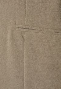 Beiger Stoff mit einer strukturierten Oberfläche, der auf der rechten Seite ein gestepptes Taschen-Detail aufweist und eine saubere, glatte Oberfläche hat.