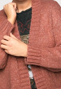 Rust-colored cardigan with a chunky knit design, featuring a ribbed texture, wide sleeves, and an open front style.