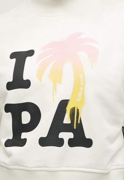 Λευκή μπλούζα με μεγάλο μαύρο κείμενο "I PA" και ένα ροζ-κίτρινο δακρυσμένο φοίνικα που αντικαθιστά το γράμμα "L" στη λέξη "PALM".